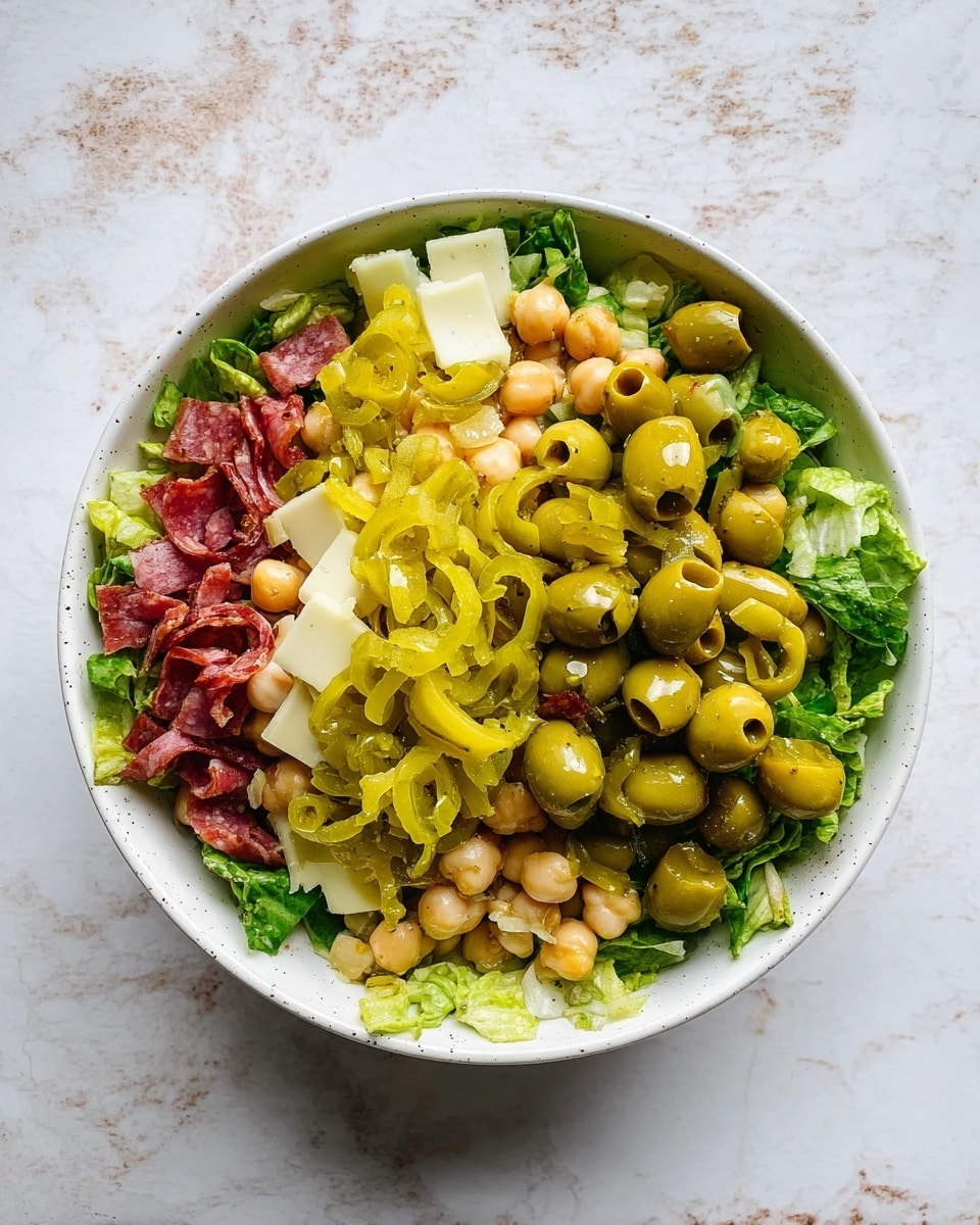 A white bowl filled with a fresh salad sits on a white marbled surface. The salad has several layers: the bottom is green leafy lettuce giving a textured, leafy look; scattered on top are light yellow ring-shaped pepper slices and pale beige chickpeas that add round shapes. Small, white rectangular cheese pieces are spread evenly, along with thin red strips of salami adding a touch of reddish color. Green olives are mixed throughout, giving small round shapes with a glossy finish. A bronze-colored spoon rests on the right side of the bowl. Photo taken with an iphone --ar 4:5 --v 7