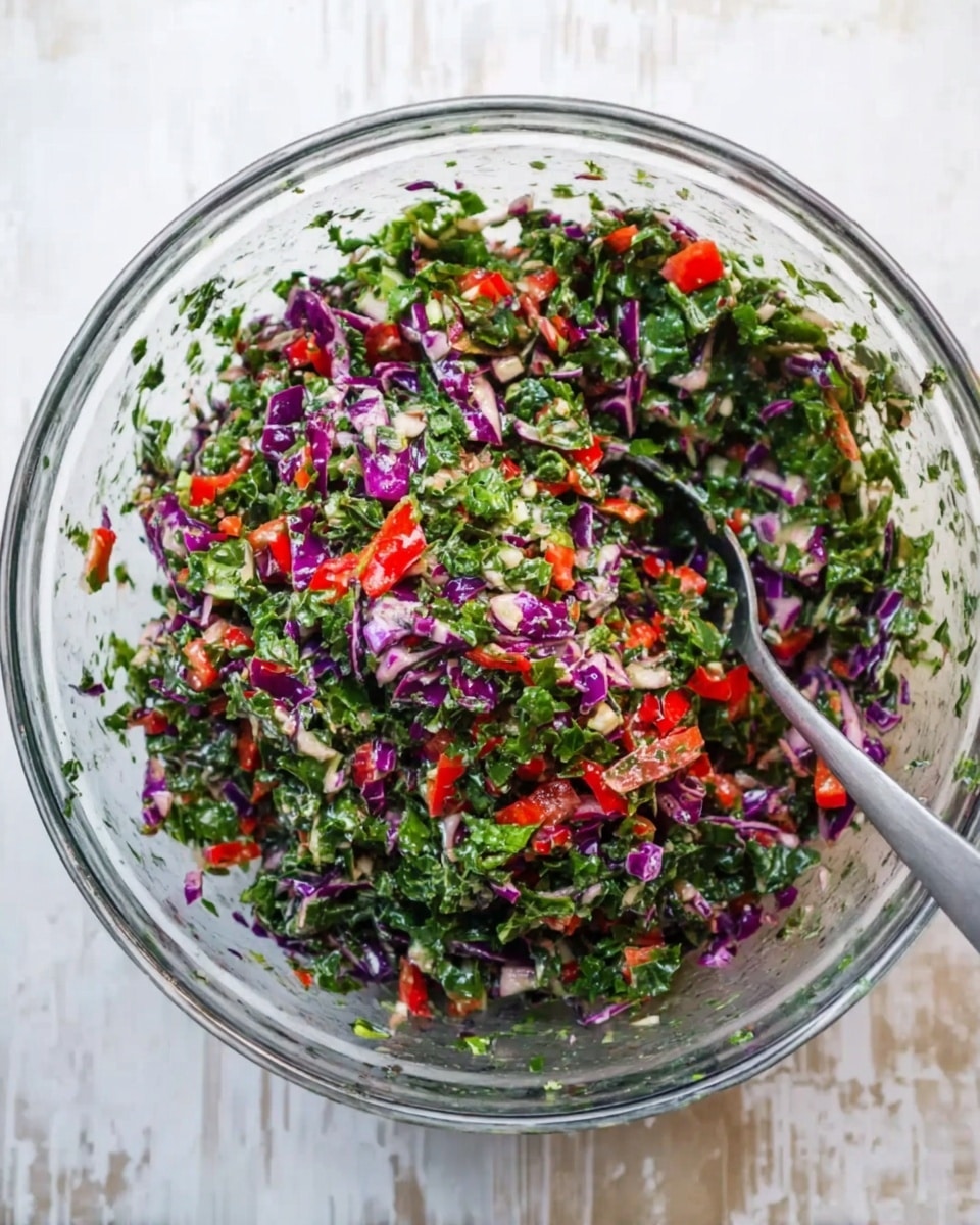 A clear glass bowl filled with a colorful salad consisting of finely chopped bright green leafy vegetables, small pieces of red bell pepper, and shredded purple cabbage. The textures vary from crunchy cabbage to tender leafy greens, all mixed together evenly. A silver spoon rests inside the bowl, slightly buried in the salad. The bowl is placed on a white marbled surface, adding a clean and light background to the vibrant salad. photo taken with an iphone --ar 4:5 --v 7