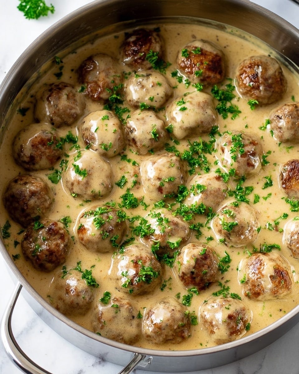 The image shows a white bowl filled with a dish of creamy mashed potatoes on one side and several brown meatballs covered in light brown gravy on the other side. The mashed potatoes look smooth and soft with a fork pressing into them from the side of the bowl. The meatballs are round with a slightly rough texture and are sprinkled with small bits of green herbs. The gravy is thick and creamy, coating both the meatballs and some parts of the mashed potatoes. The bowl sits on a white marbled surface, and only a small green plant is slightly visible in the background near the top left corner. photo taken with an iphone --ar 4:5 --v 7