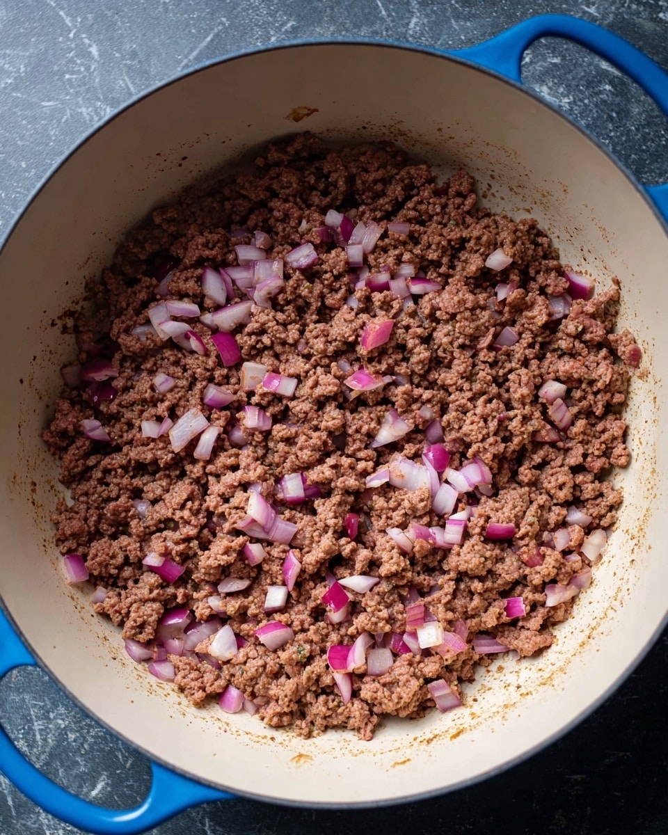 A large blue pot with a light tan inside is filled with cooked ground meat mixed with small cubes of red and white onion. The meat is brown and crumbly, evenly spread out in the pot, with bits of onion scattered throughout. The pot sits on a dark surface, which is changed to a white marble texture in the description. The overall look is rustic and simple, showing the cooked mixture ready for the next step in making a dish. Photo taken with an iphone --ar 4:5 --v 7