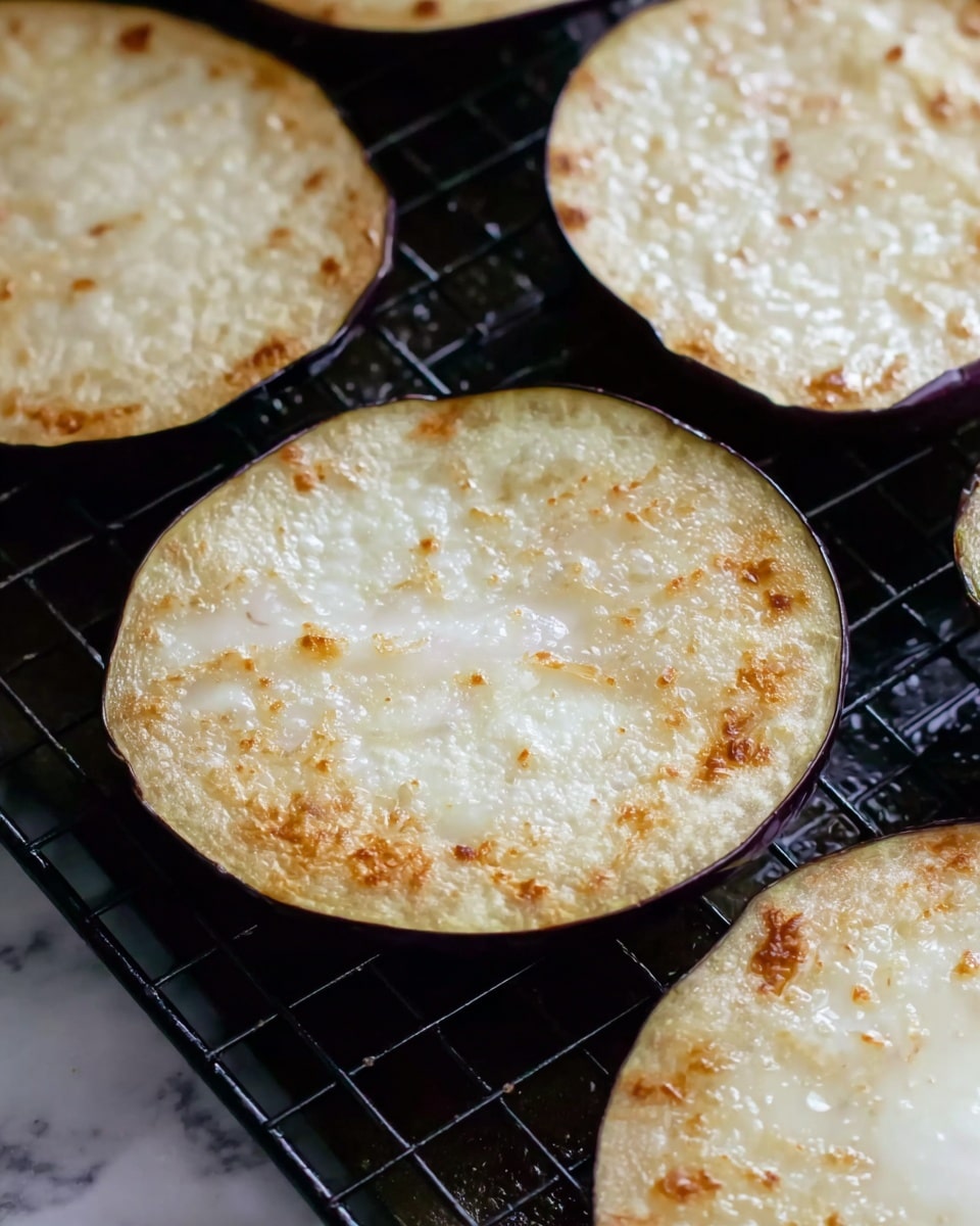 The image shows several round slices of eggplant with a light golden-brown surface on a black grill rack. Each slice has a slightly bubbly texture from cooking, with some light browning spots scattered unevenly across the pale cream-colored flesh. The purple edges of the eggplant slices frame the soft, cooked centers, creating a contrast between the darker skin and lighter interior. The grill rack is set on a white marbled surface, adding brightness to the scene. Photo taken with an iphone --ar 4:5 --v 7