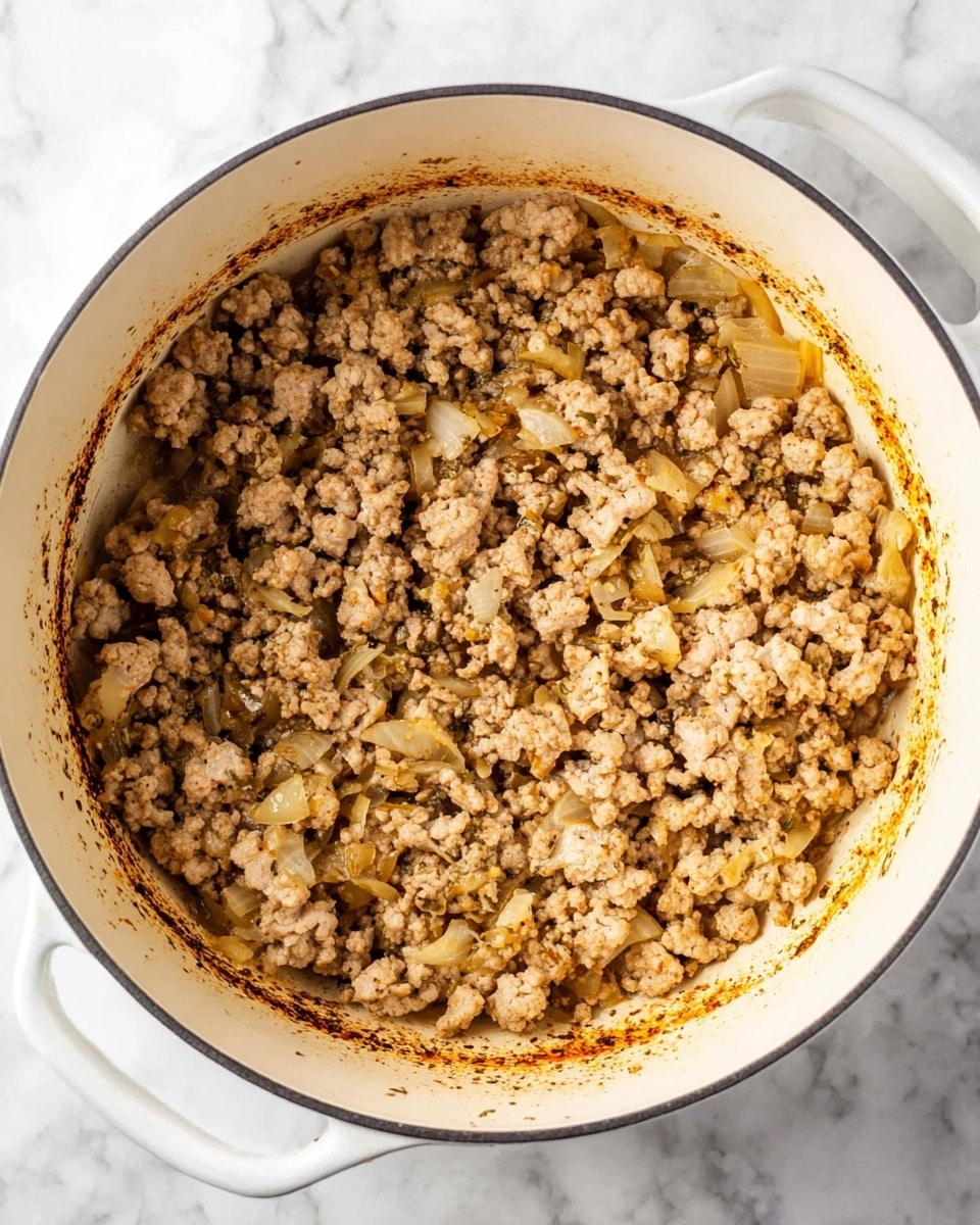 A white pot filled with cooked ground meat mixed with small chopped onions. The meat is crumbly and light brown, with some pieces slightly darker. The onions are soft and pale yellow, scattered evenly throughout the meat. The inside rim of the pot has some browned bits from cooking. The pot is placed on a white marbled surface. photo taken with an iphone --ar 4:5 --v 7