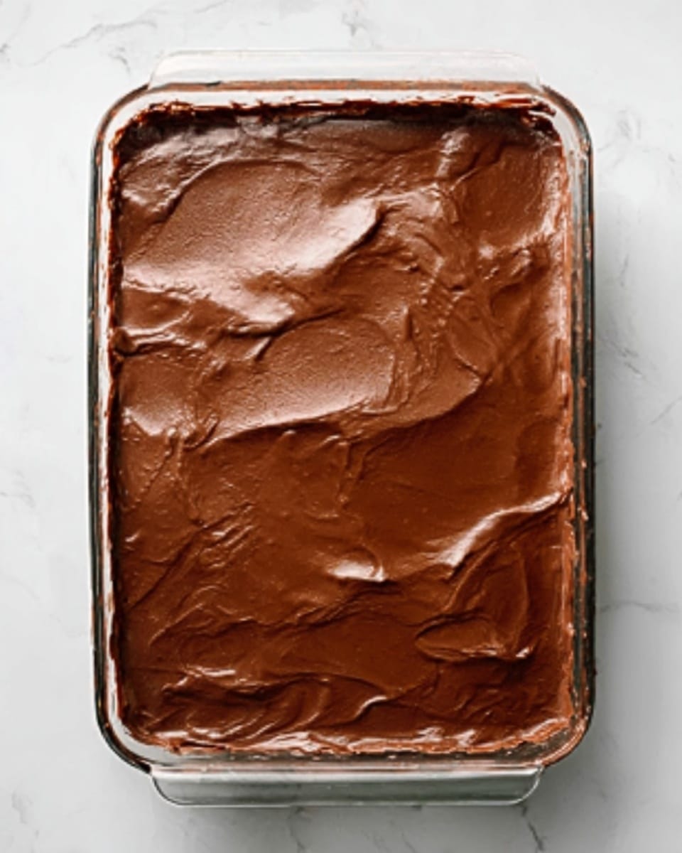 The image shows a glass rectangular dish filled with a thick, smooth chocolate layer covering the entire surface evenly, with a few soft waves and slight shiny spots from the chocolate. The dish rests on a white marbled surface, making the rich brown color of the chocolate stand out clearly. photo taken with an iphone --ar 4:5 --v 7