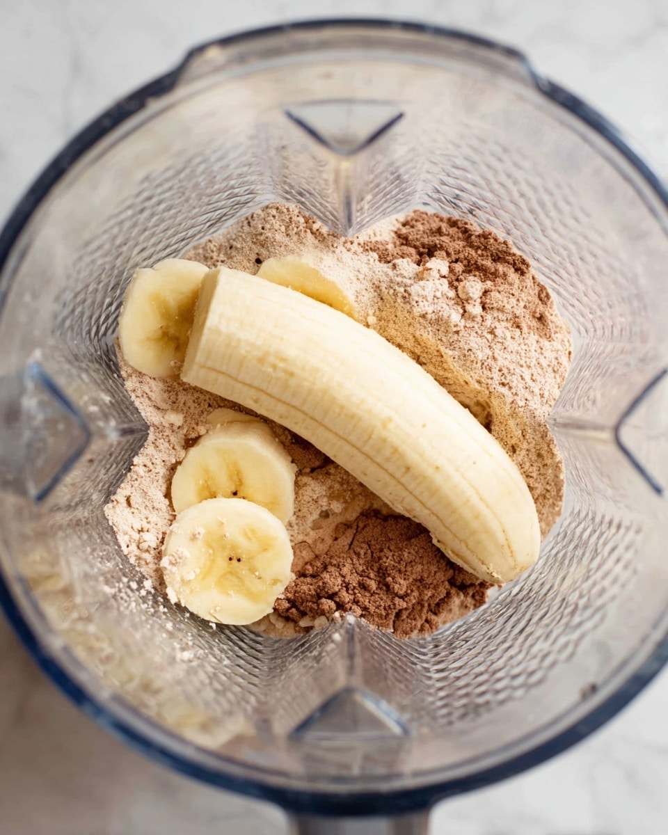 Inside a clear blender, there are three main layers: the bottom layer is a light brown powdery mix, spread around the edges. On top of this mix, two peeled bananas lay side by side, one more aligned vertically and the other horizontally, showing a soft yellow color with slight brown spots. The blender’s textured glass walls reflect light, and the whole scene sits on a white marbled surface. photo taken with an iphone --ar 4:5 --v 7