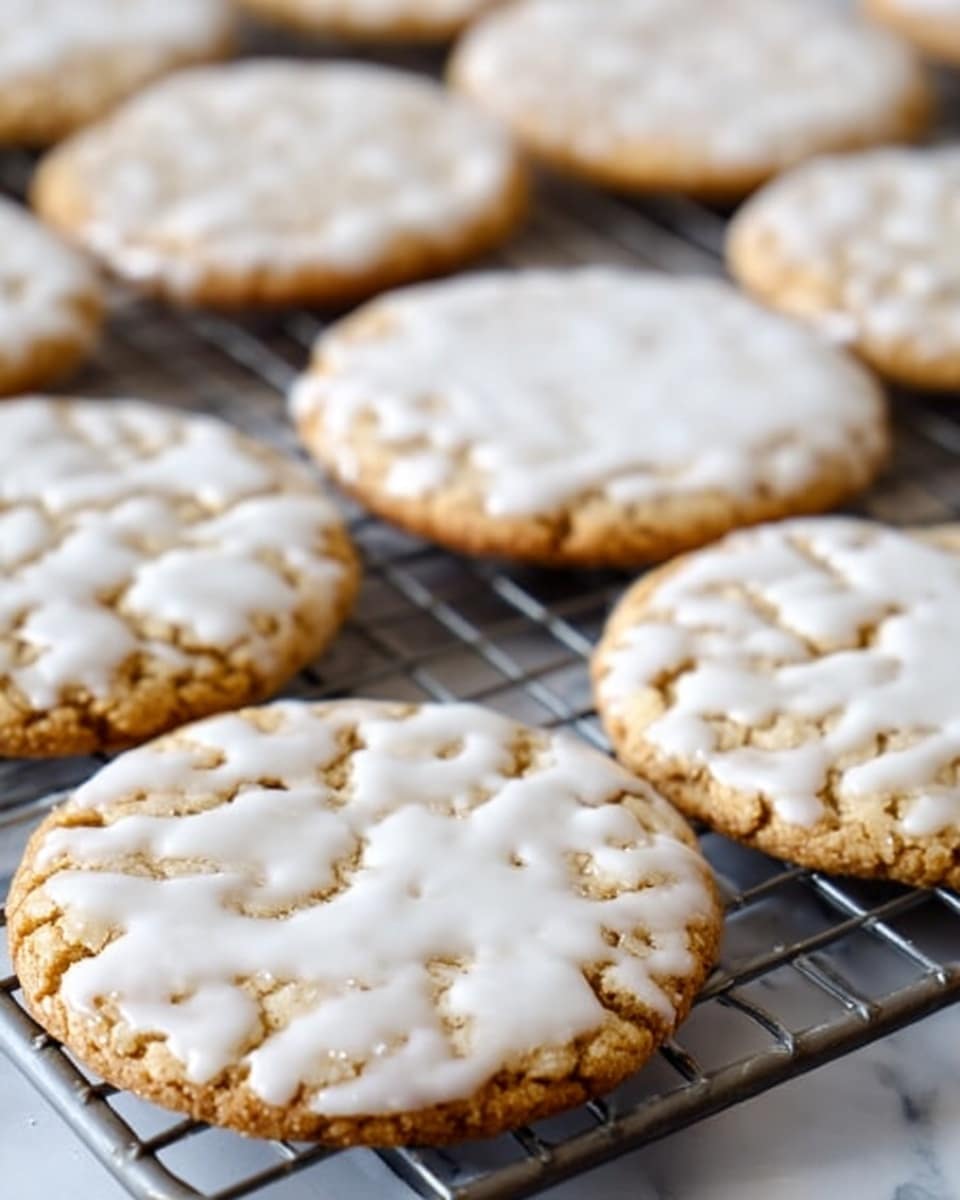 The image shows multiple thin round cookies with white icing spread unevenly on top, giving a cracked texture. The cookies are light brown underneath with the icing covering most but not all of each cookie’s surface. They sit on a grey cooling rack, which is placed on a white marbled surface. The cookies are arranged close but not touching, filling most of the frame. The lighting is soft, highlighting the shiny icing and the rough cookie texture below. photo taken with an iphone --ar 4:5 --v 7